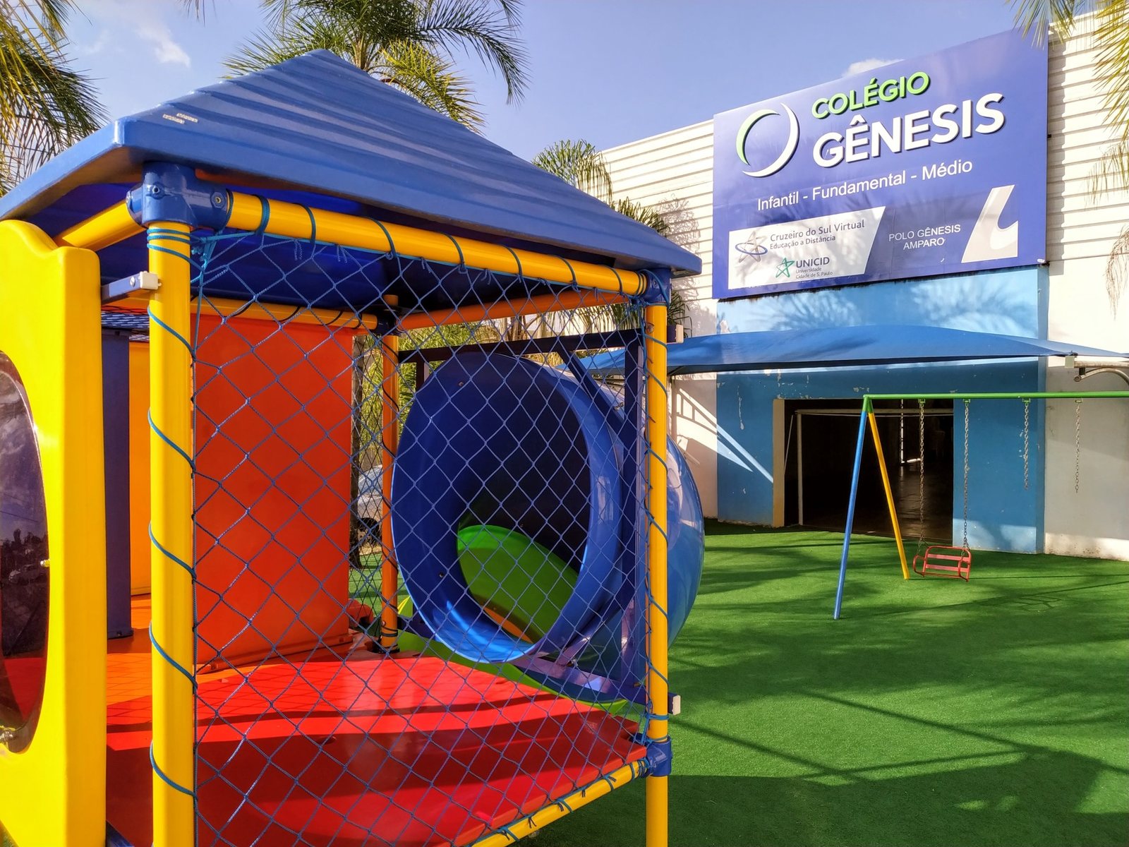 Playground do Colégio Gênesis em Amparo/SP com brinquedos coloridos e fachada da escola